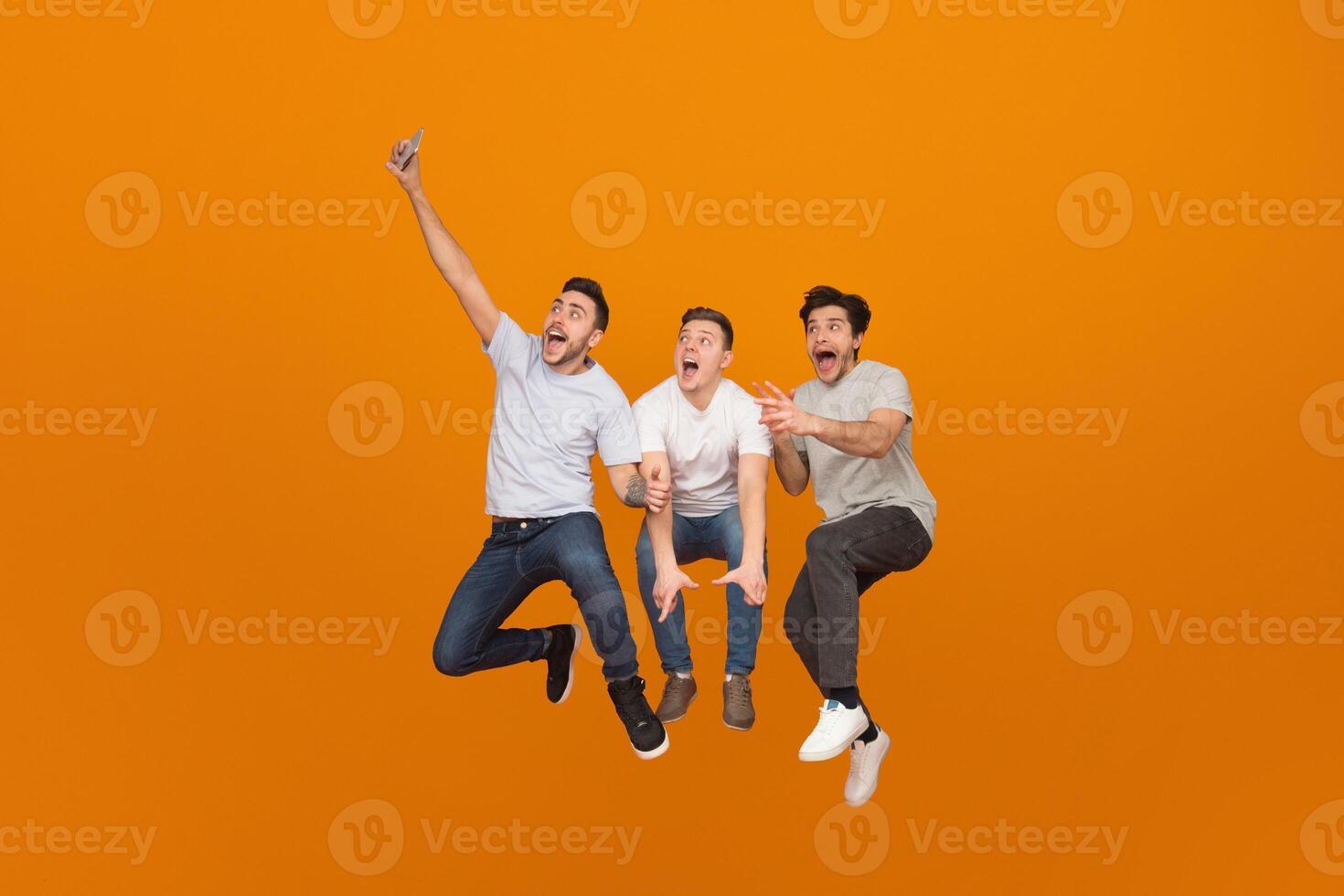 Fooling together. Men taking selfie when jumping on orange studio background photo
