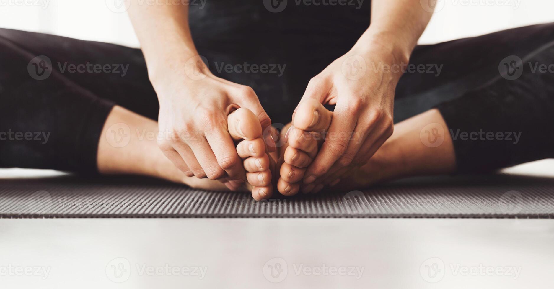 Cropped of woman is seated on a yoga mat in a cross-legged position, gently pulling their toes forward as part of a stretching routine, panorama photo