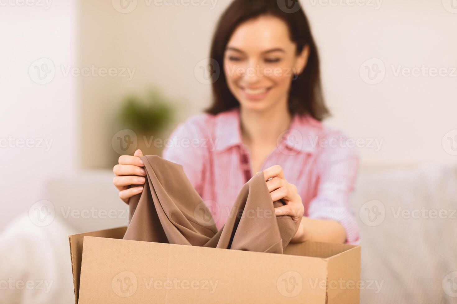 Woman packaging gift for her friend in a cardboard carton, putting clothes in box, close up, selective focus photo