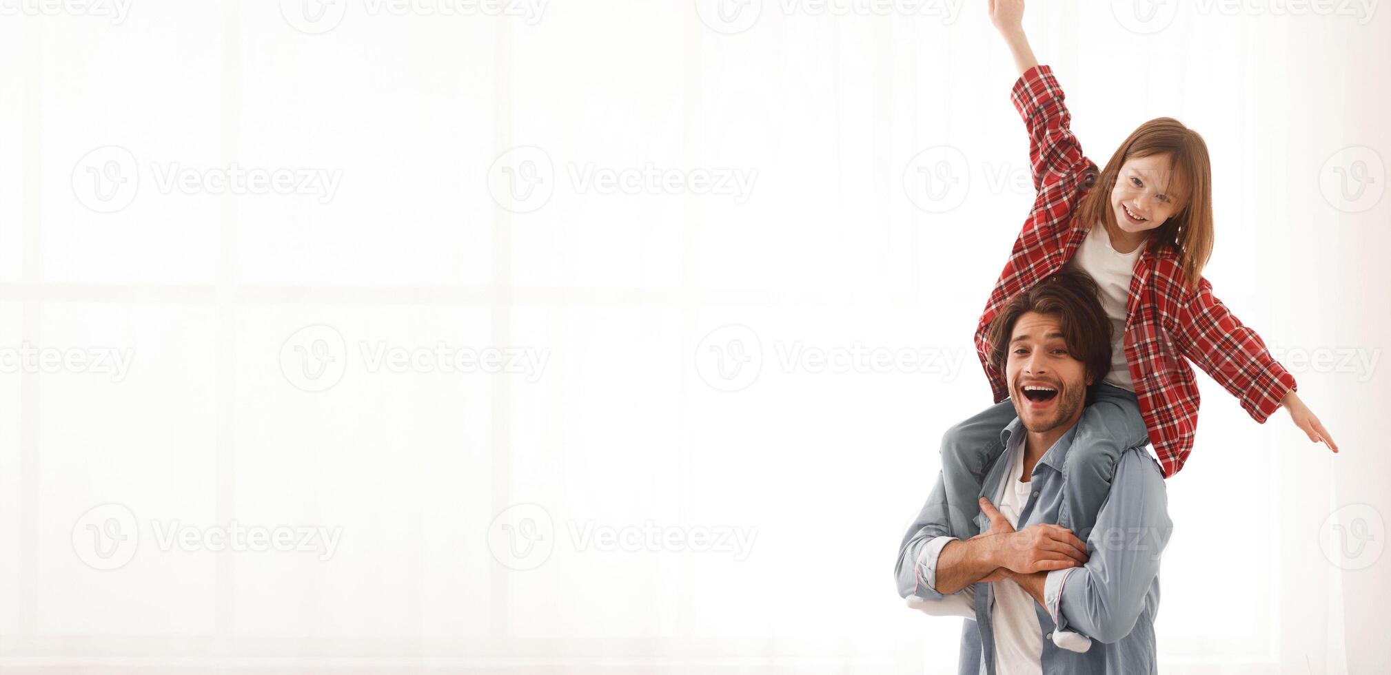 Joyful father and little daughter having fun over white background at home, girl sitting on dad shoulders, happy family concept, copy space photo