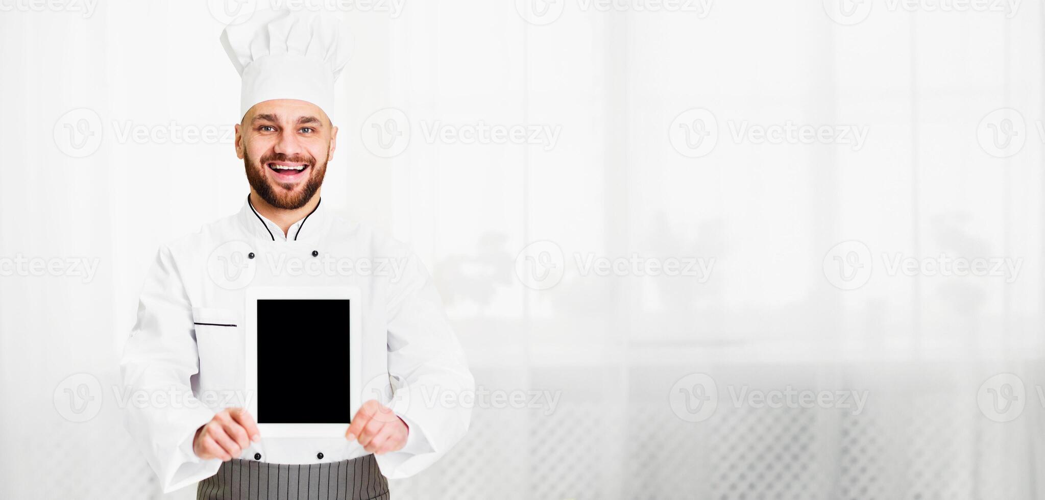 Culinary Recipes App. Chef Cook Man Holding Blank Digital Tablet Screen With Menu Standing In Restaurant Kitchen Indoor. Mockup photo