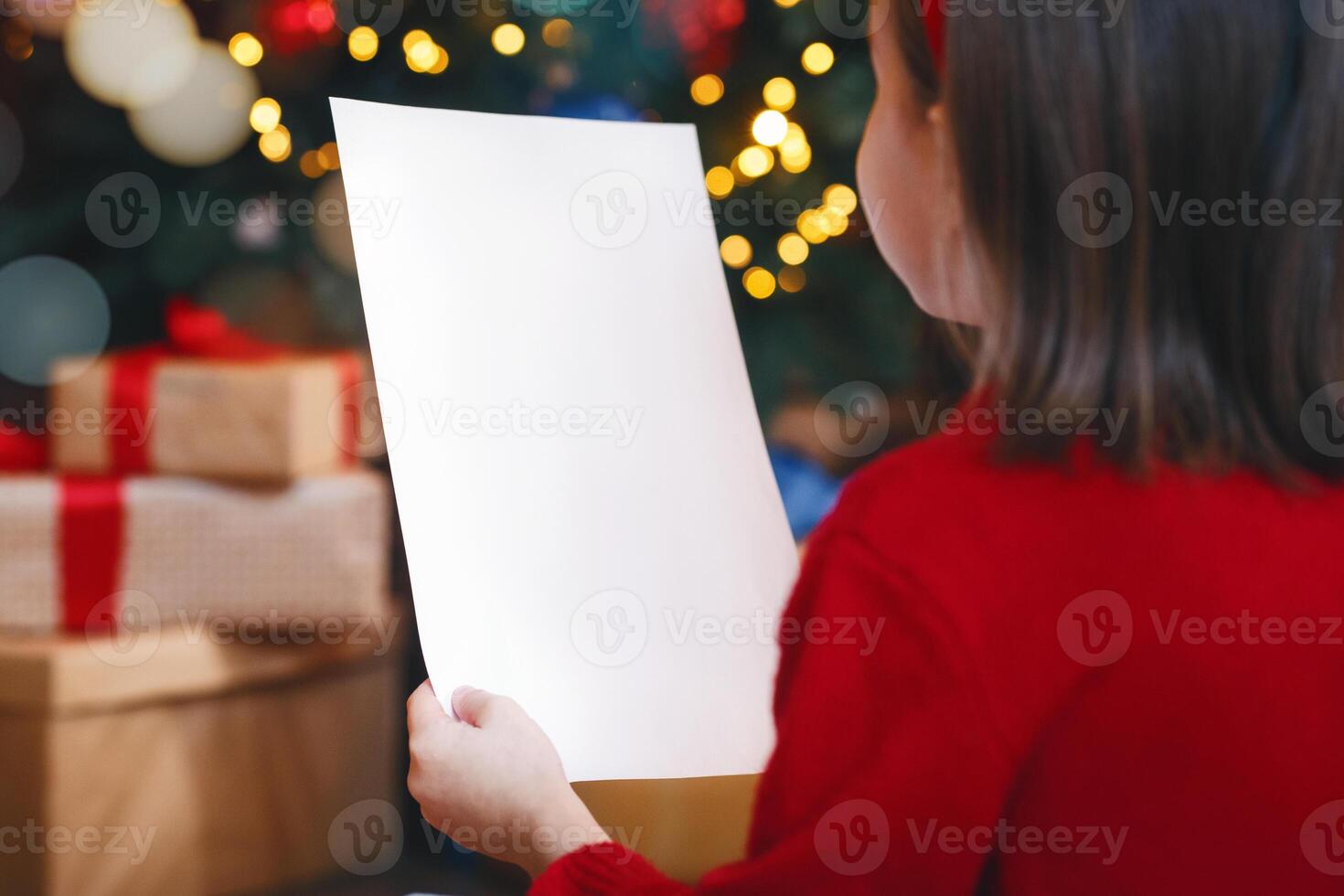 Back view of little girl holding blank white empty paper over Christmas festive background, mockup, free space photo