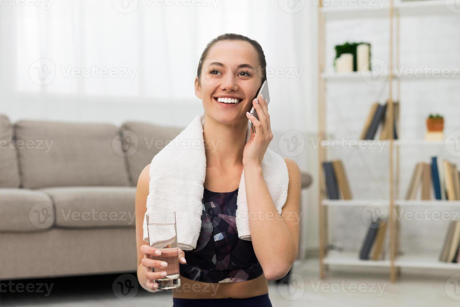 Fit girl talking on phone after exercising at home, drinking water and having rest, free space photo