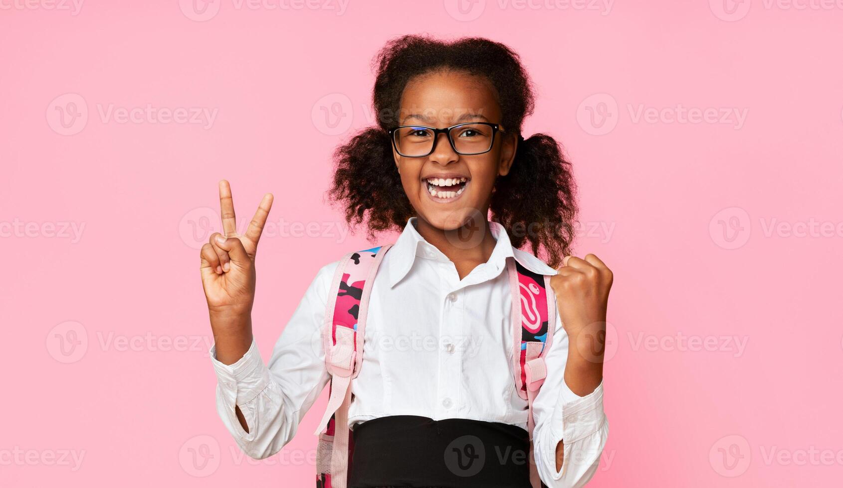 Excited Black Elementary School Girl Gesturing Victory Sign On Yellow Studio Background. Little Winner Concept photo