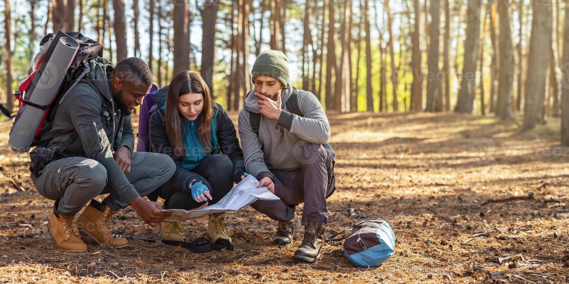 Lost backpackers looking for location, using map, international group hiking in forest, copy space photo