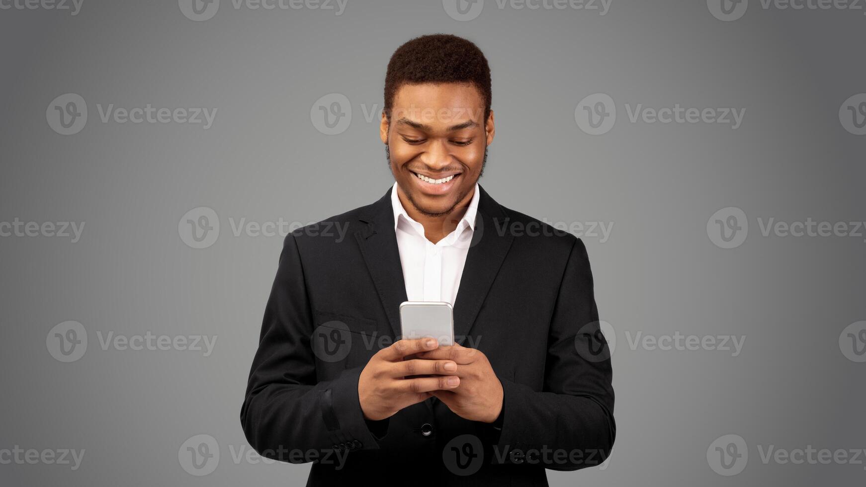 Online Chat. Happy black guy in suit using mobile phone, texting email to clients, white background, panorama photo