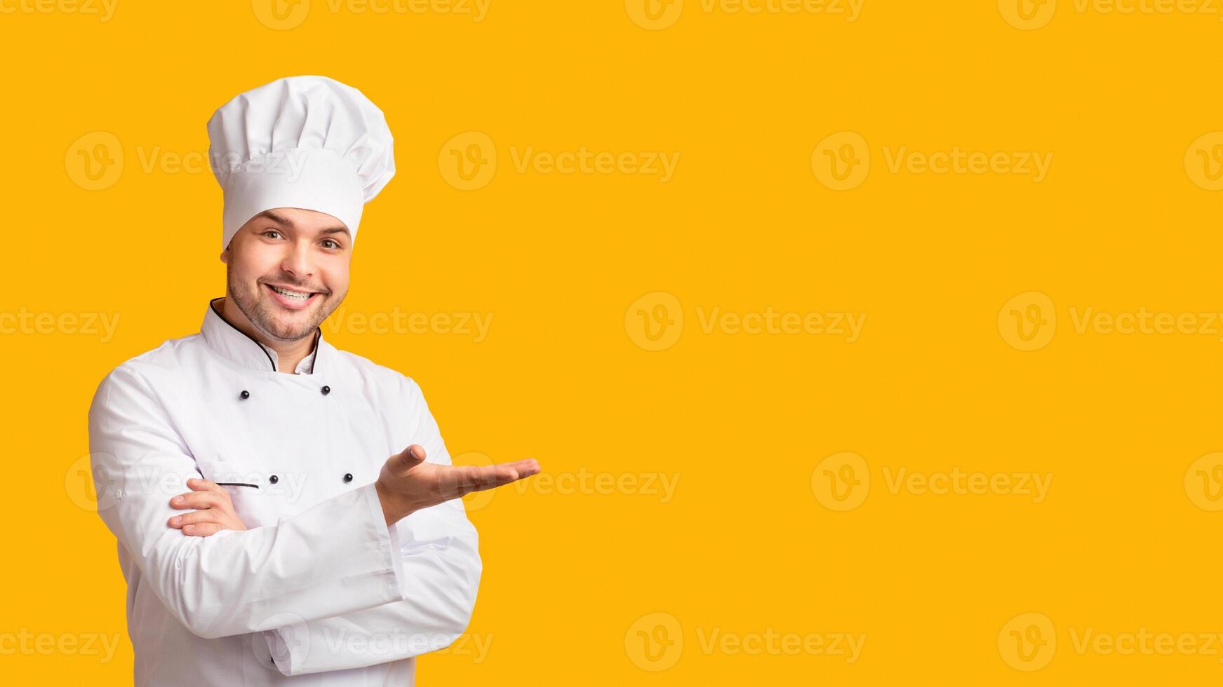 Restaurant Chef. Professional Cook Man Gesturing With Hand Showing Something Standing Over Yellow Studio Background. Panorama With Free Space photo