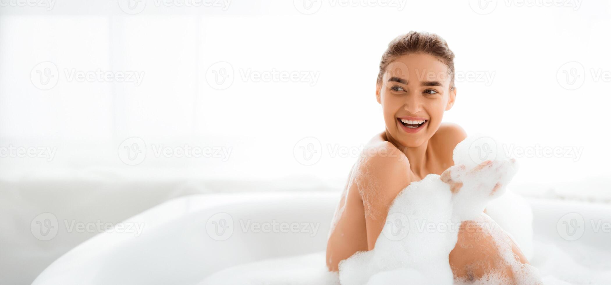Joyful girl relaxing in bath with foam , laughing and having fun, copy space photo