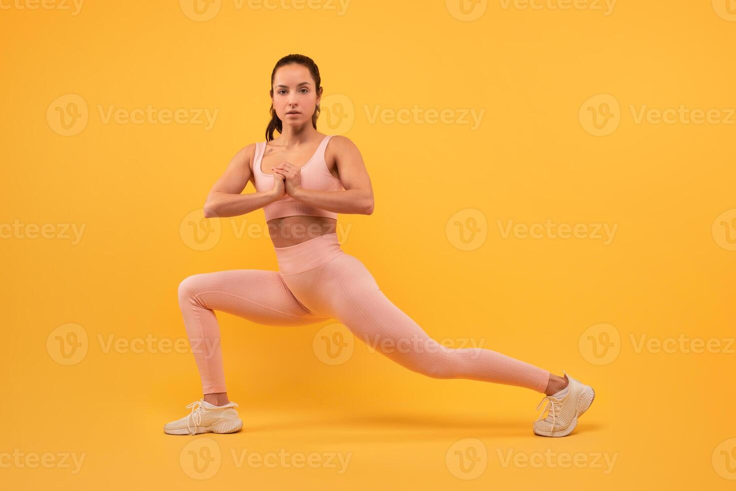 A woman dressed in a pink outfit is focused and balanced as she practices a yoga pose. Her body is aligned, and she displays strength and flexibility in her movement. photo