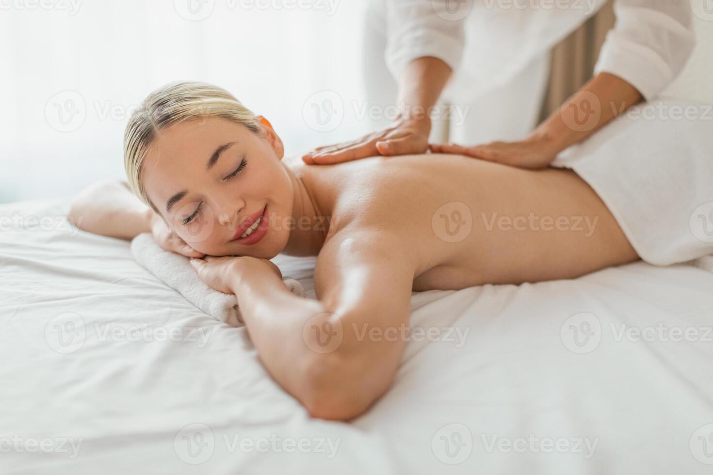 Blonde woman is lying face down on a massage table in a spa, while a massage therapist is massaging her back using steady pressure. photo