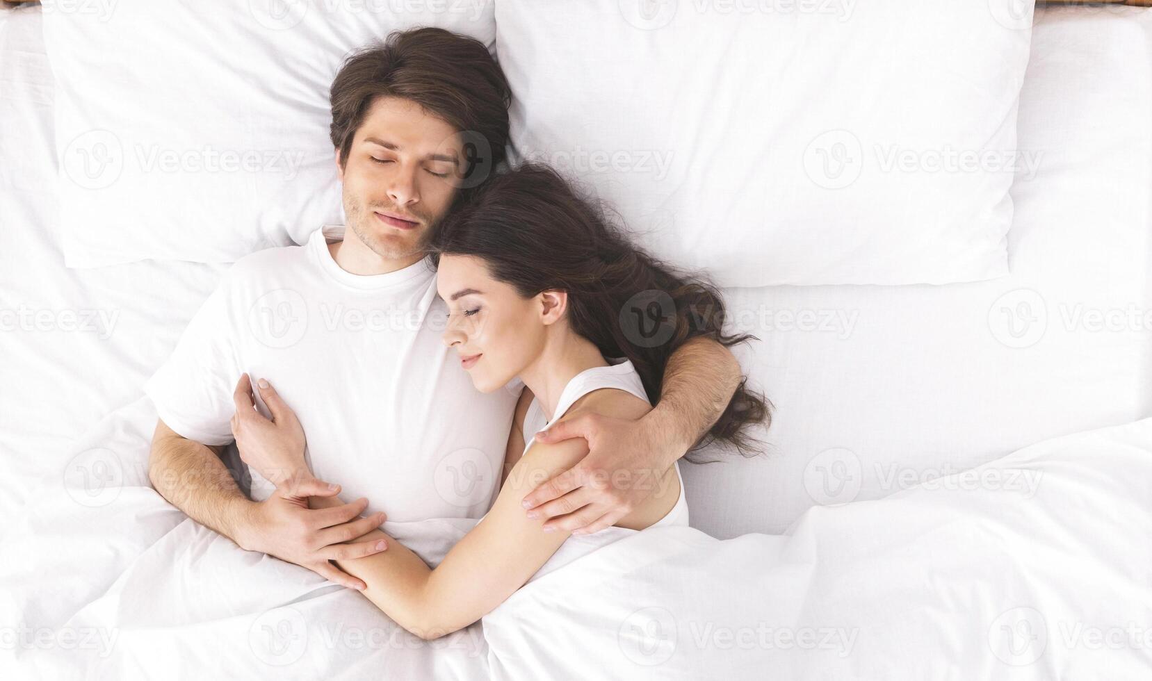 Loving millennial couple sleeping in bed in morning and hugging, love and relationships concept, top view, free space photo