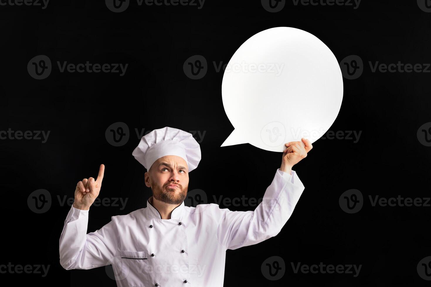 Funny Chef Man Holding Empty White Speech Bubble Pointing Finger Up Having Idea Posing Over Black Background. Studio Shot, Mockup photo