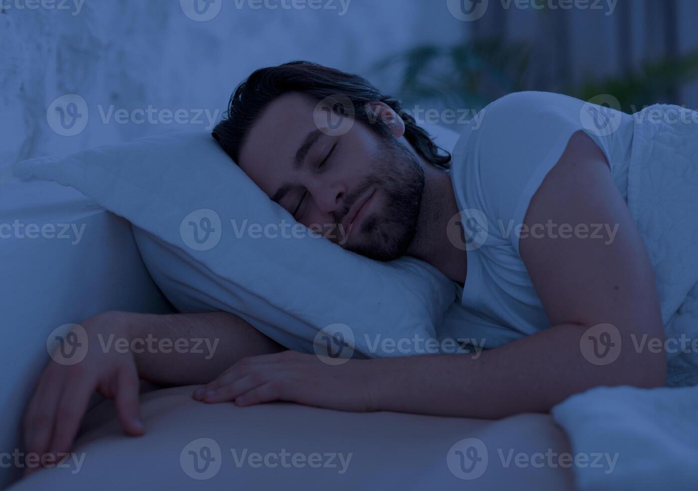 Peaceful handsome bearded young man sleeping in comfortable bed alone at home, enjoying his orthopedic mattress and pillow, side view, copy space. Good sleep concept photo