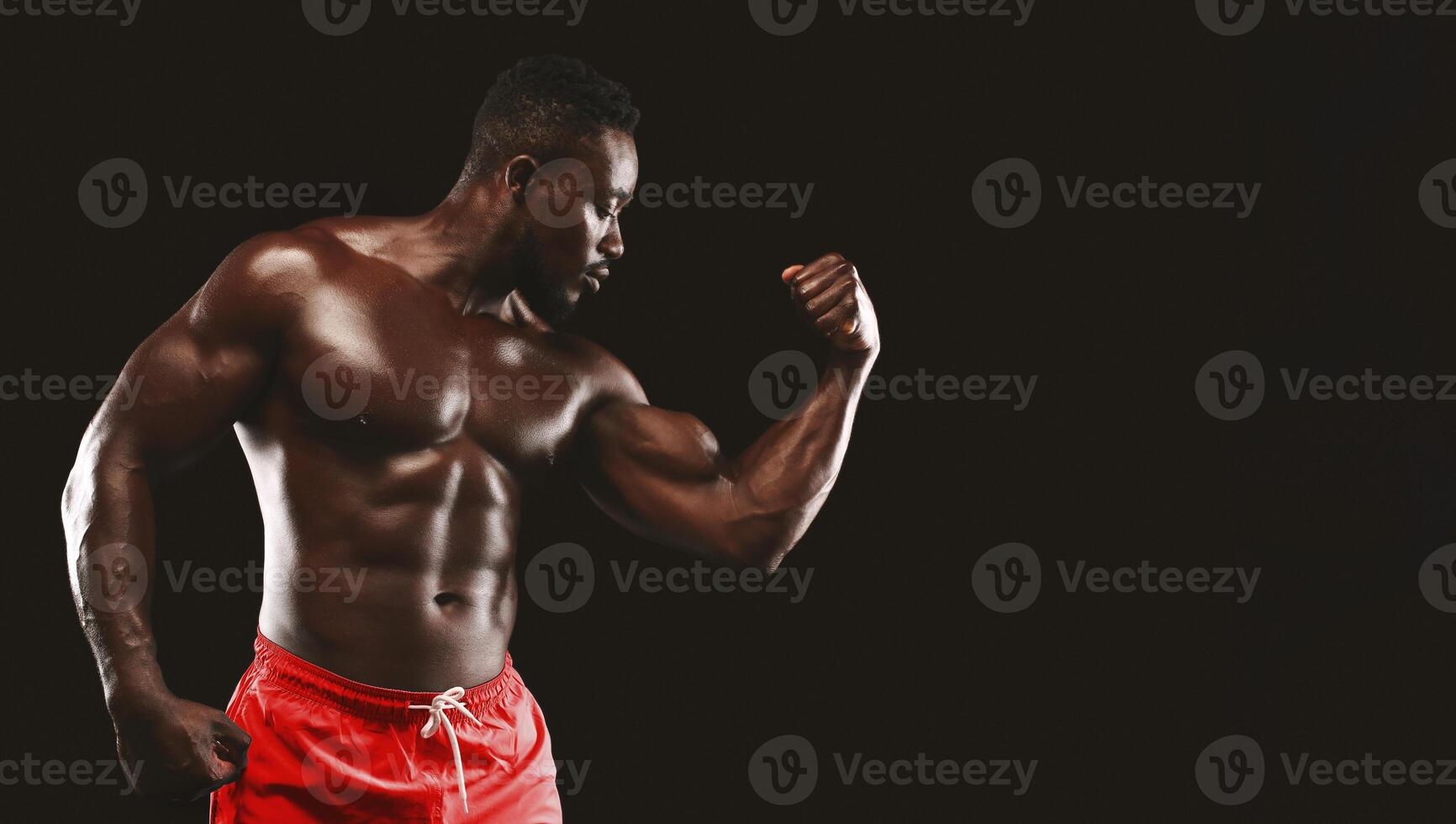 A muscular man with a defined physique flexes his bicep against a black background. photo