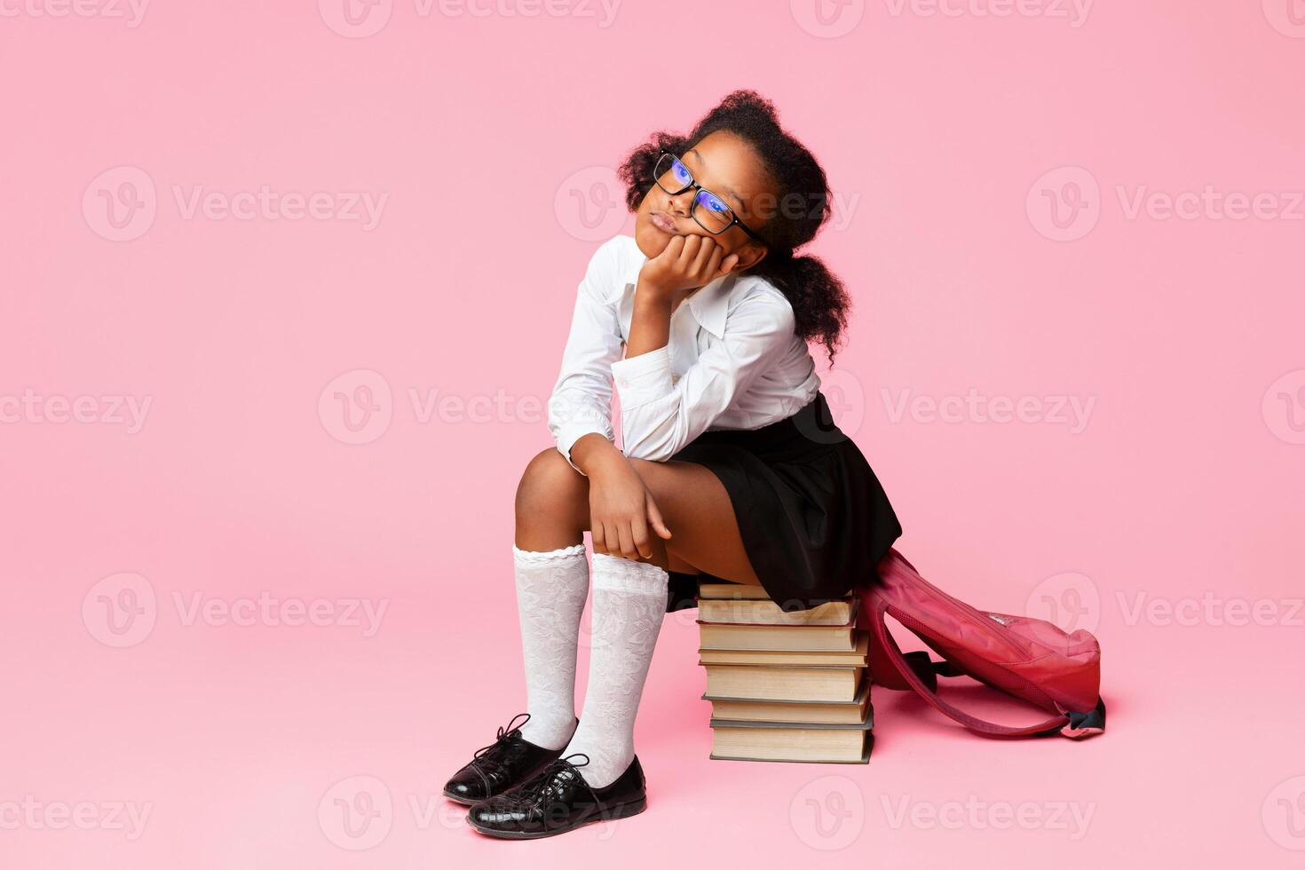 School Homework Concept. Bored Afro Schoolgirl Sitting On Stack Of Books Over Yellow Studio Background. Empty Space photo