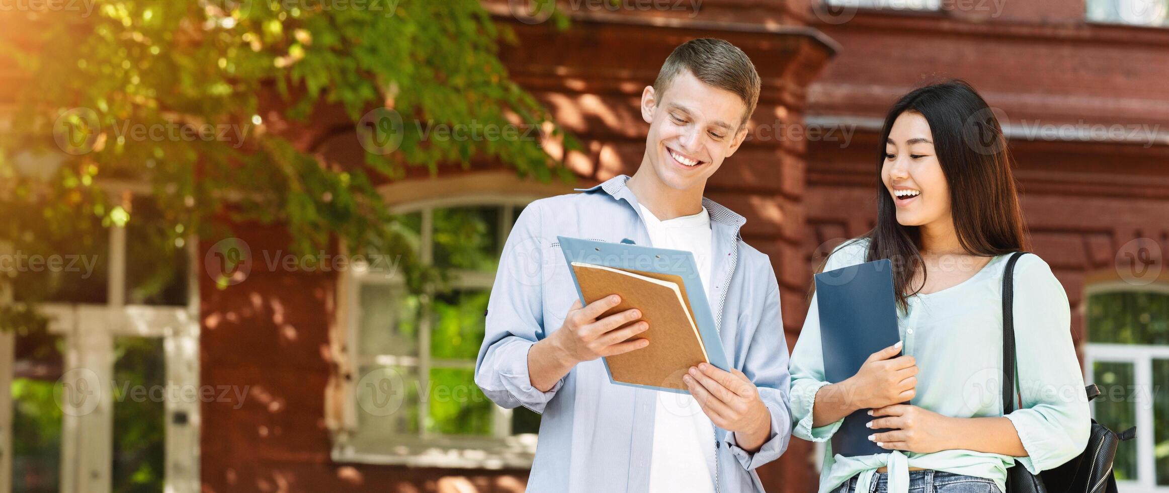 Student couple going to college class, checking lessons schedule outdoors and laughing, standing in university campus photo
