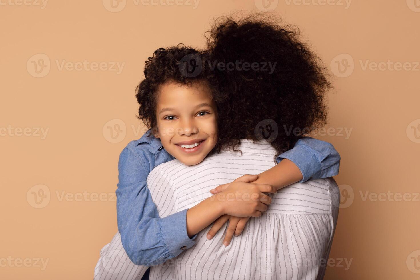 A young African American boy with curly hair smiles brightly as he embraces a woman, presumably his mother, demonstrating a moment of affection and closeness photo