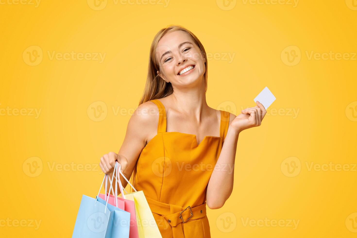 Loyalty Program Concept. Happy Young Woman Holding Shopping Bags And Credit Card Over Yellow Background, Received Bonus After Purchase photo