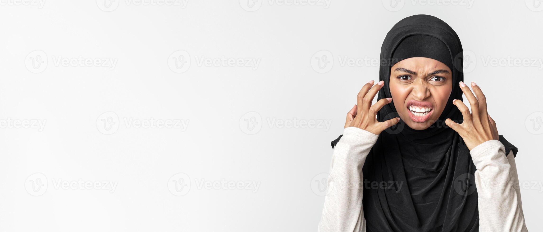 Hate Concept. Angry arabic woman in hijab emotionally grimacing and gesturing in rage and looking at camera, posing over light background, closeup photo