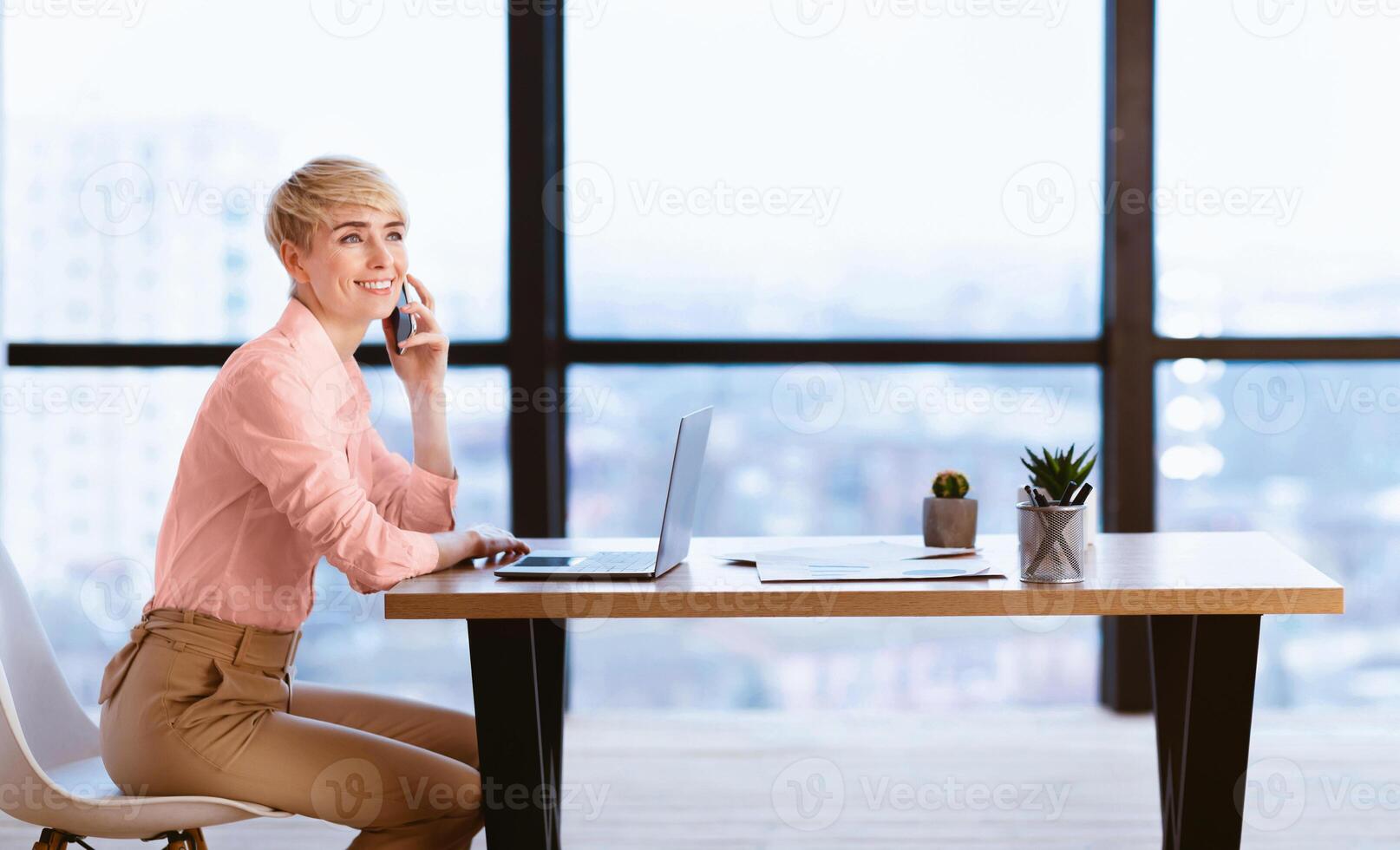 Business Lady Talking On Mobile Phone Sitting At Laptop At Workplace In Modern Office. Empty Space For Text photo