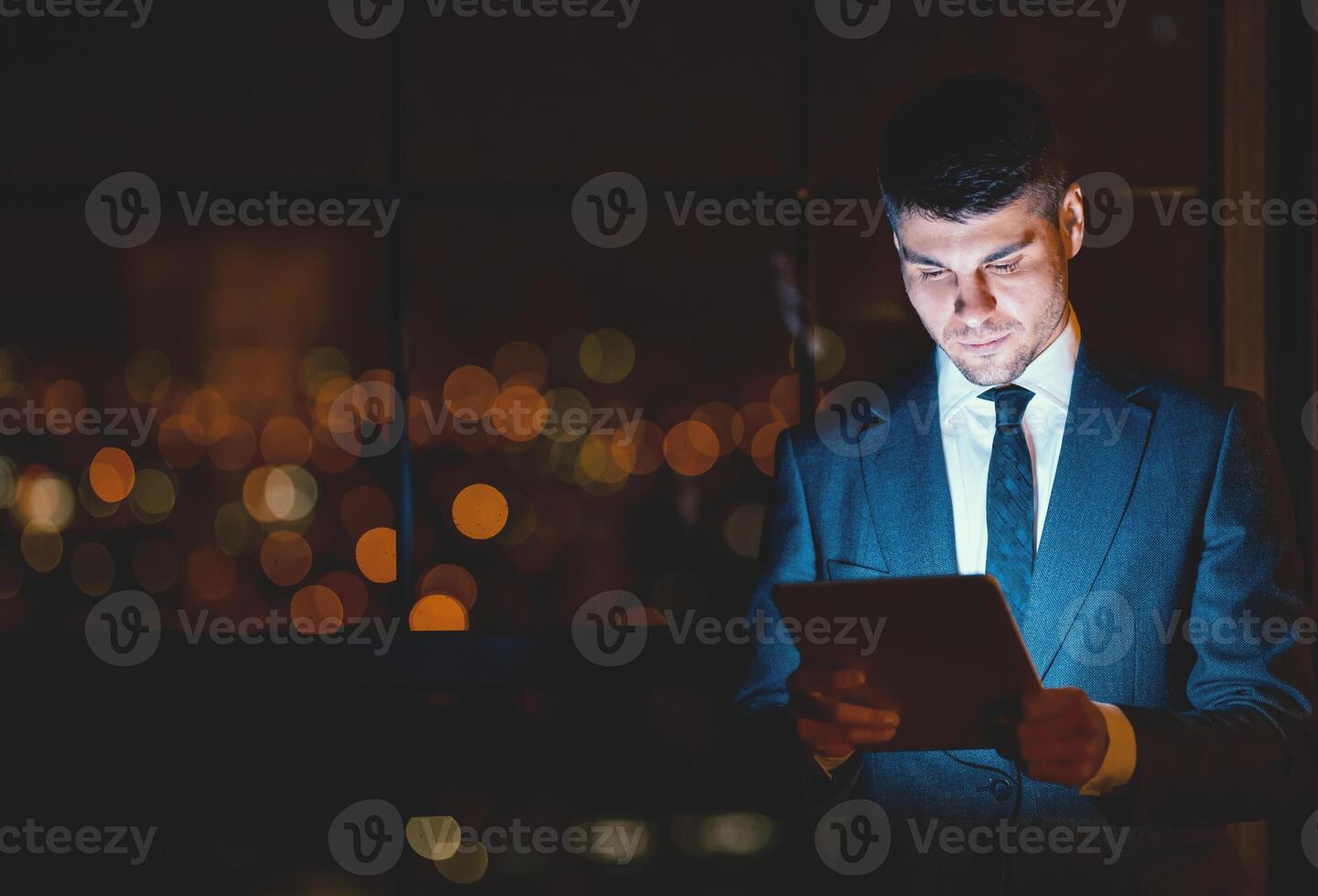 Businessman Using Digital Tablet Reading Business News Standing In Modern Office At Night. Empty Space, Low Light photo