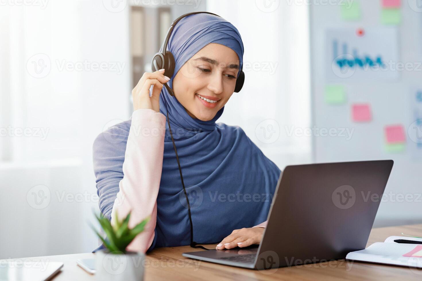 Customer Representative Service Concept. Portrait Of Smiling Female Call Center Operator In Hijab And Headset Using Laptop In Office photo