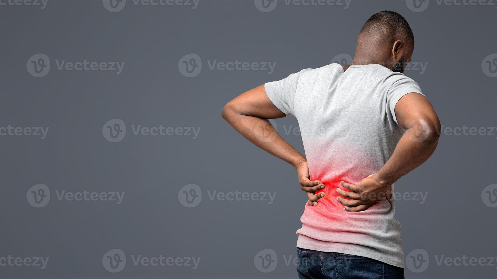 Afro guy holding both hands on lower back, pain in spine, inflamed zone highlighted in red, white background, free space photo