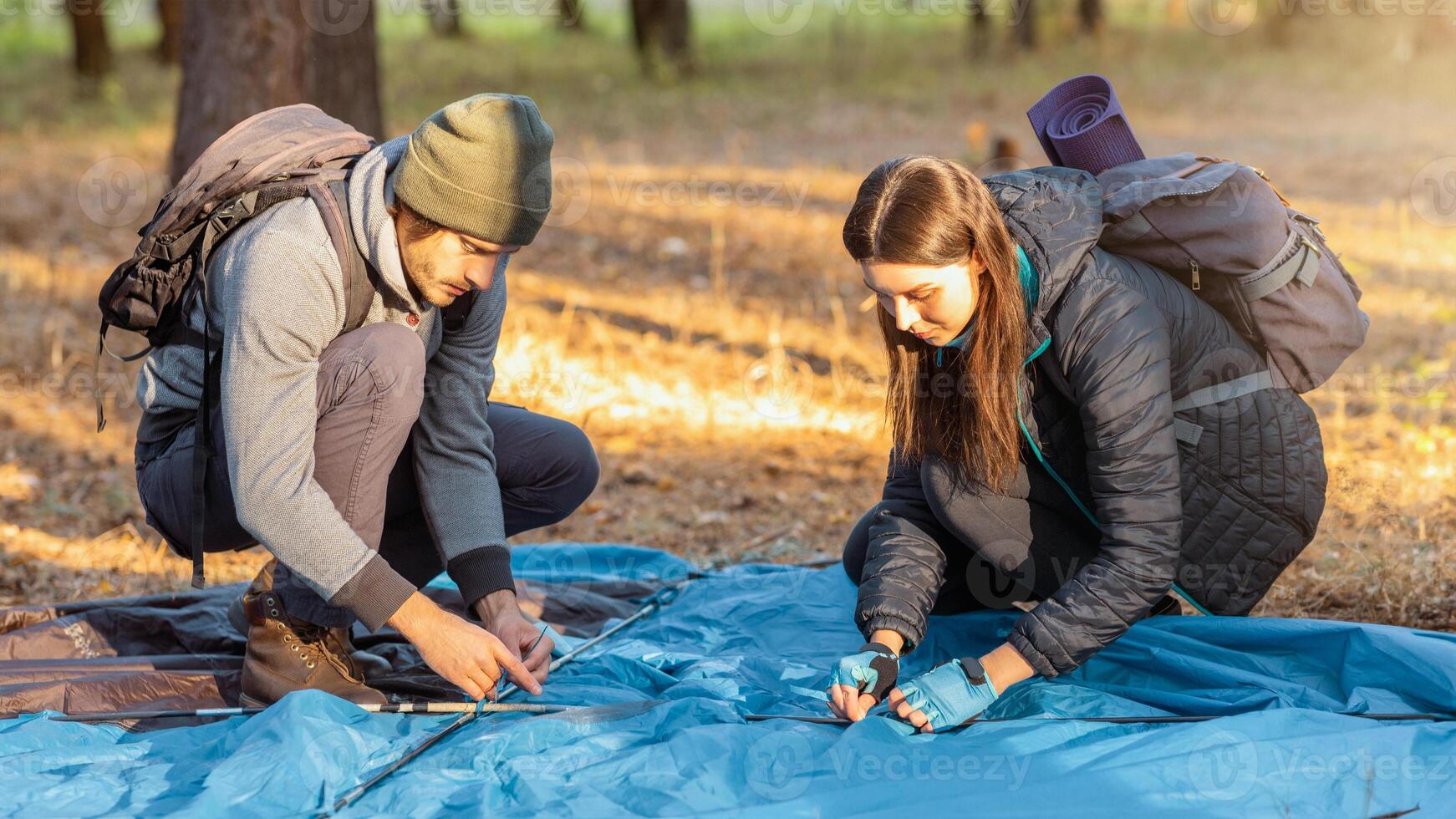 Couple of tourists pitching tent, having break in sun lights in autumn forest photo