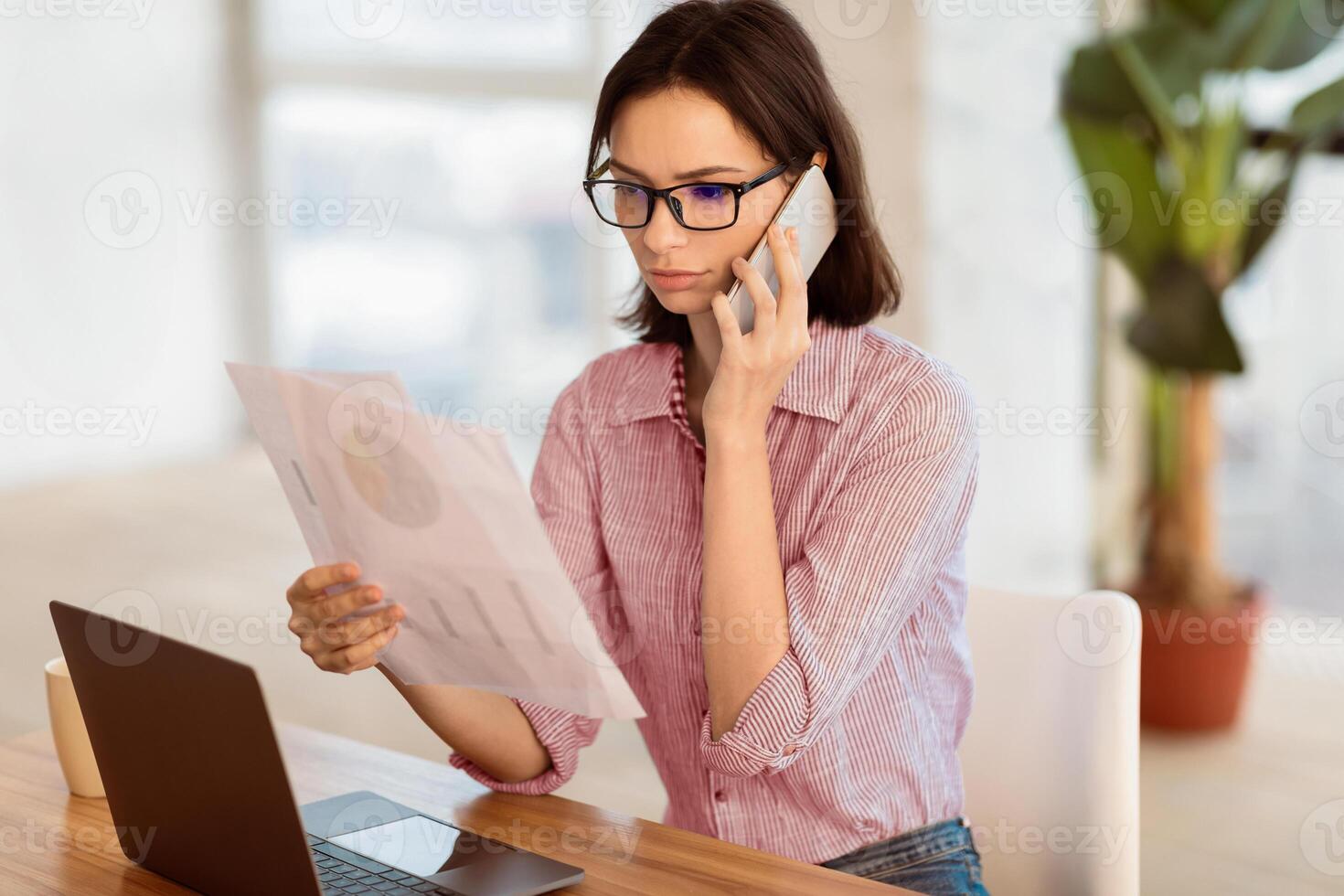 Business Concept. Serious female manager in specs making phone call and holding papers with graphs, free space photo