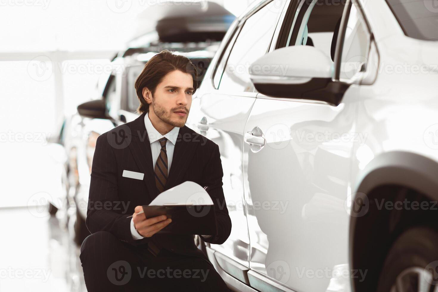 Writing Report. Serious handsome male assistant sitting near car and filling insurance form photo