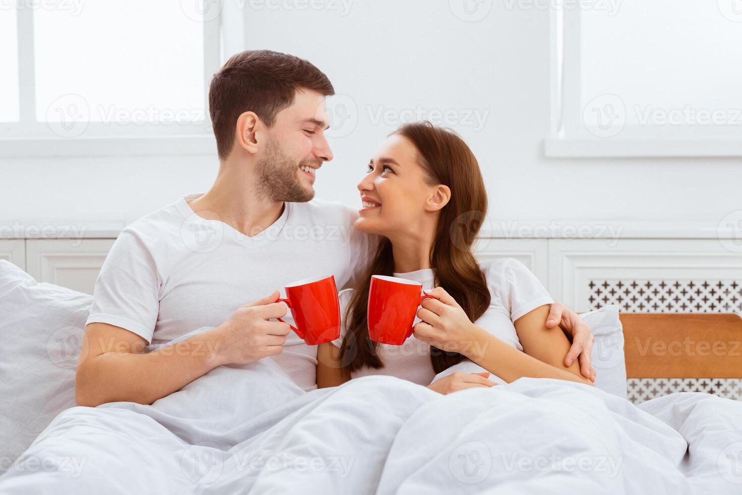 Good Morning. Happy Couple Having Coffee Hugging Lying In Bed At Home. photo