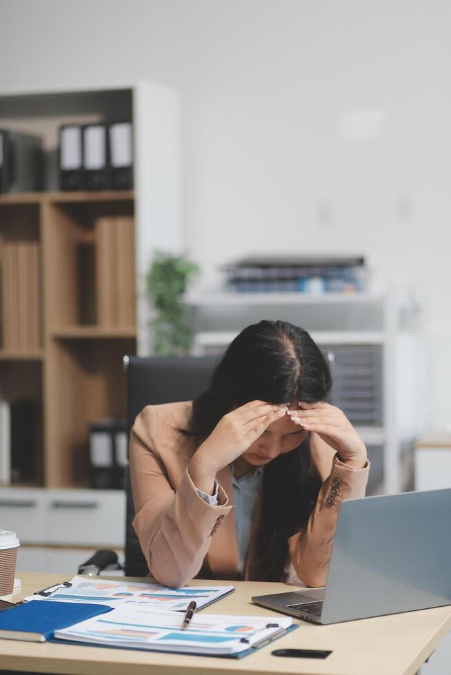 Portrait of tired young business Asian woman work with documents tax laptop computer in office. Sad, unhappy, Worried, Depression, or employee life stress concept photo