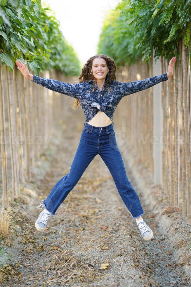 A Joyful Young Woman is Joyfully Jumping in a Vineyard Surrounded by Lush Green Rows photo