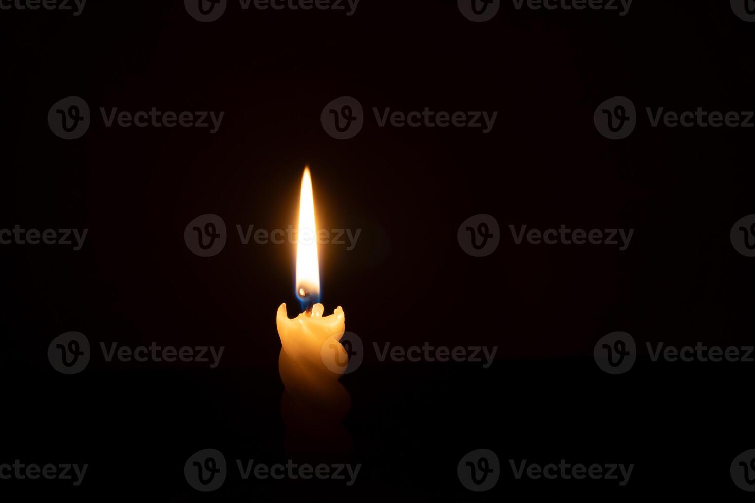 A single burning candle flame or light glowing on a spiral white candle on black or dark background on table in church for Christmas, funeral or memorial service with copy space photo