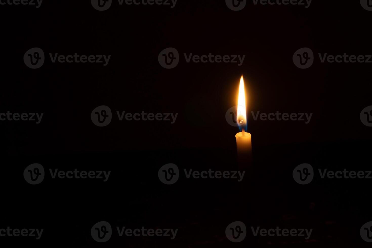 A single burning candle flame or light glowing on a small orange candle on black or dark background on table in church for Christmas, funeral or memorial service with copy space photo