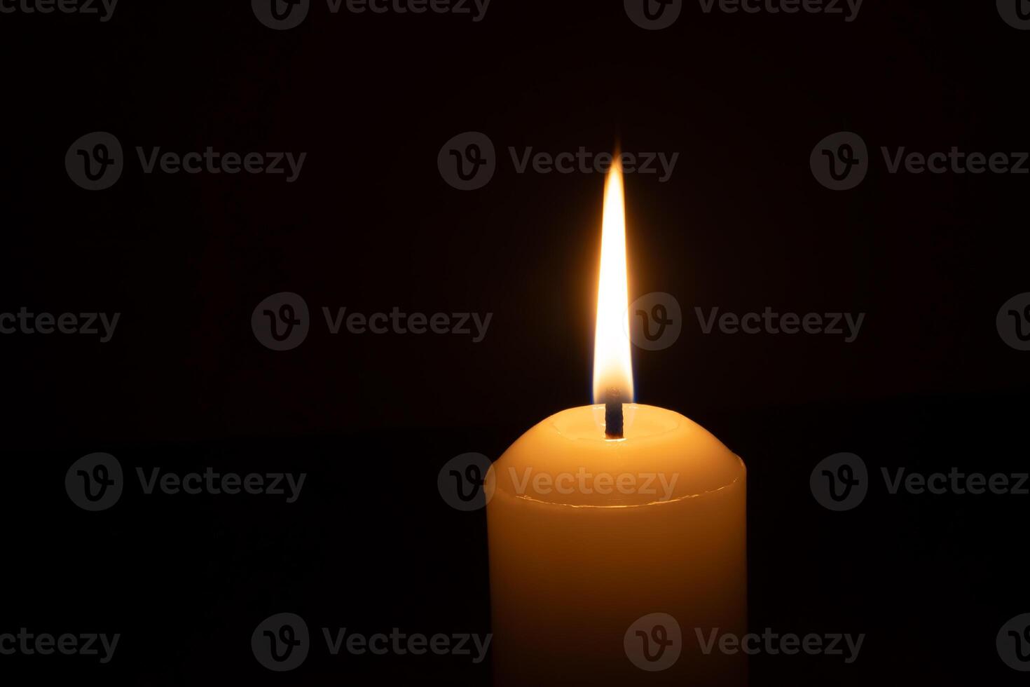 A single burning candle flame or light glowing on a big white candle isolated on red or dark background on table in church for Christmas, funeral or memorial service photo