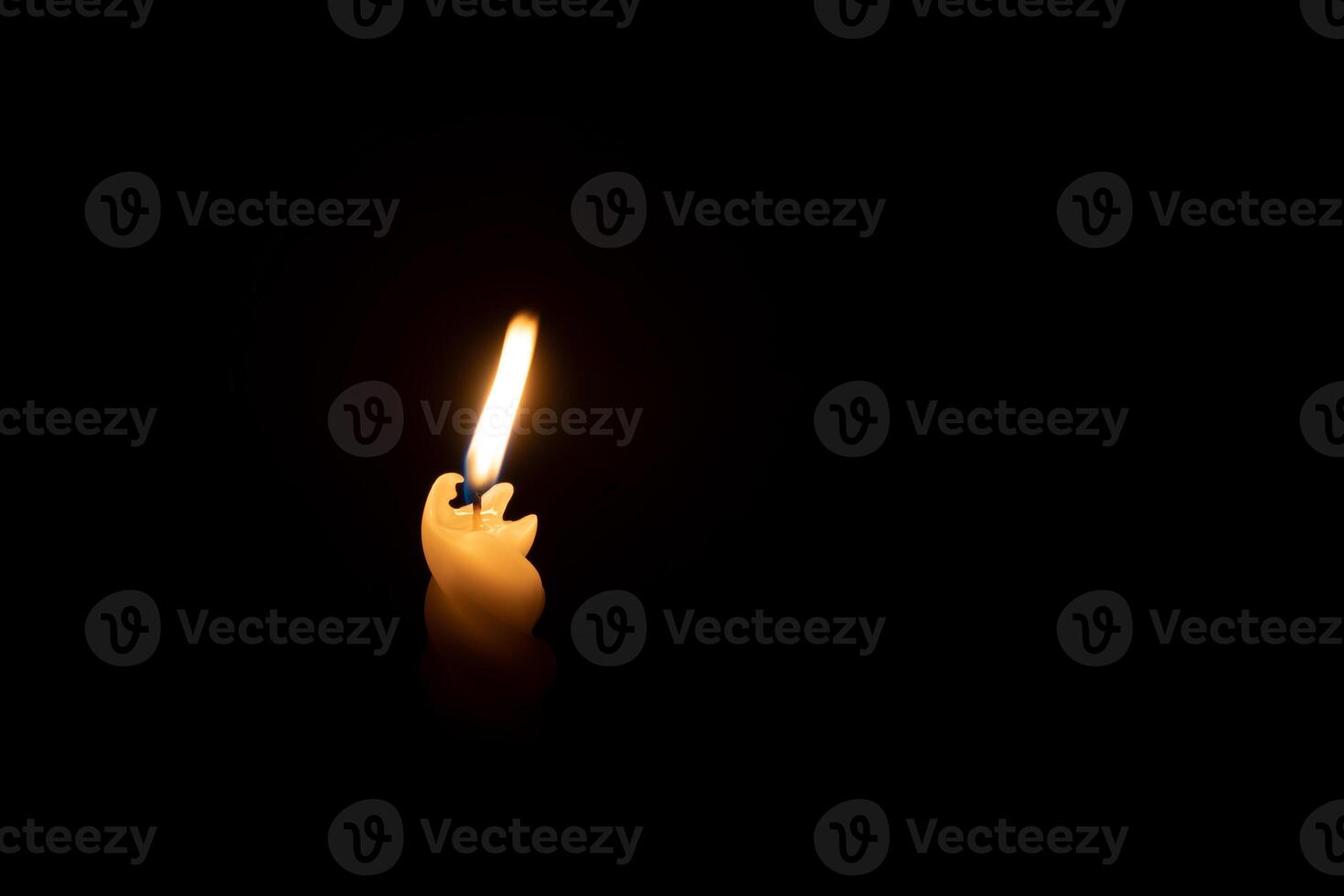 A single burning candle flame or light glowing on a spiral white candle on black or dark background on table in church for Christmas, funeral or memorial service with copy space photo