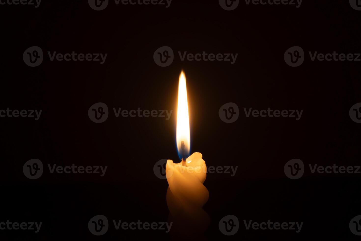 A single burning candle flame or light glowing on a spiral white candle on black or dark background on table in church for Christmas, funeral or memorial service with copy space photo