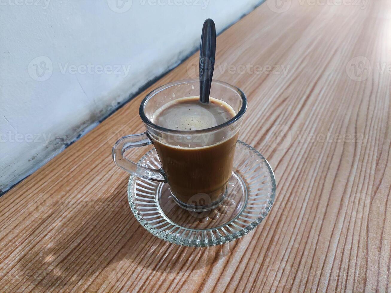 Coffee milk is stirred in a glass using a spoon on the table photo