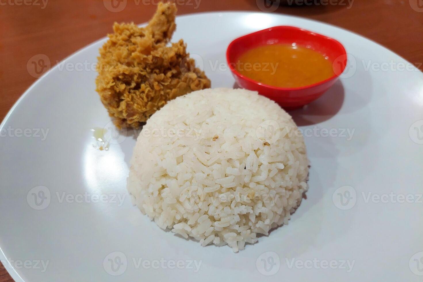 Crispy chicken, chili sauce and white rice on a white plate on the dining table photo
