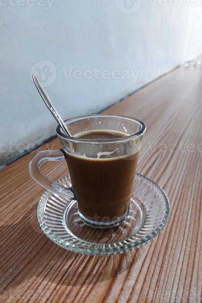 Coffee milk is stirred in a glass using a spoon on the table photo