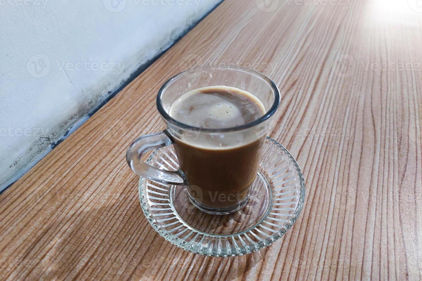 Coffee milk is stirred in a glass using a spoon on the table photo