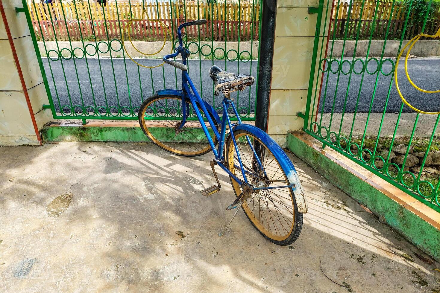An antique bicycle was parked near the fence, an old blue bicycle photo