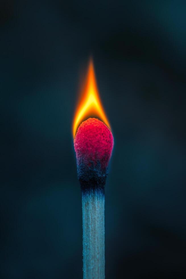 A close-up of a lit matchstick creating a vibrant flame against a dark background photo
