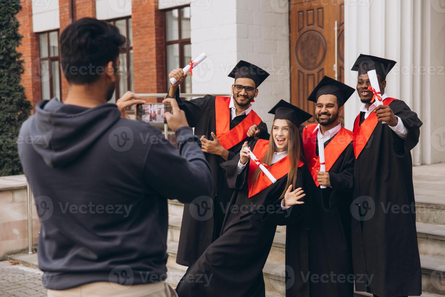 Group of Happy Graduates Celebrating Outside University with Diplomas and Taking Photos
