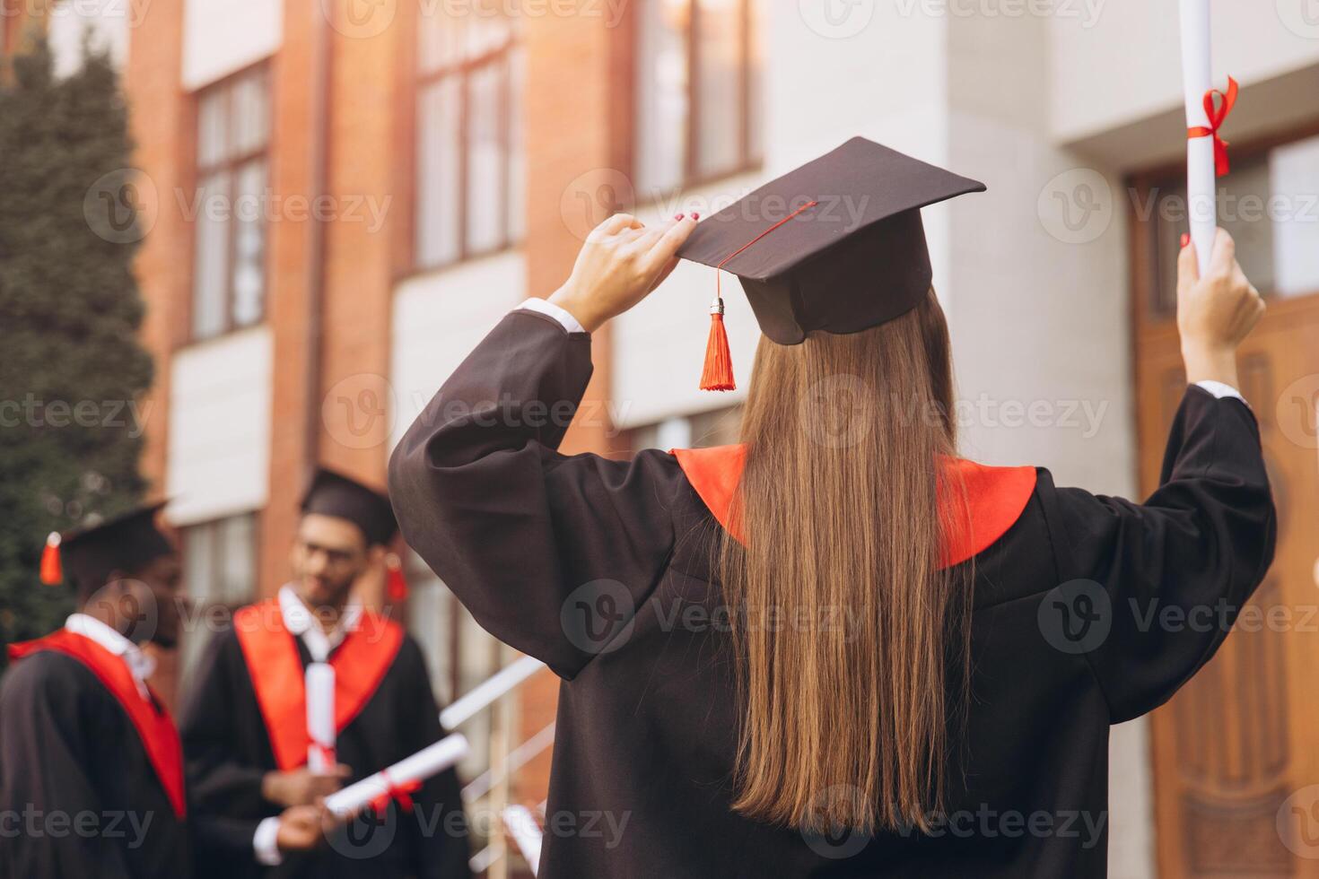 Back View Joyful Group of Graduates Celebrating Outside University Building with Diplomas and Caps photo