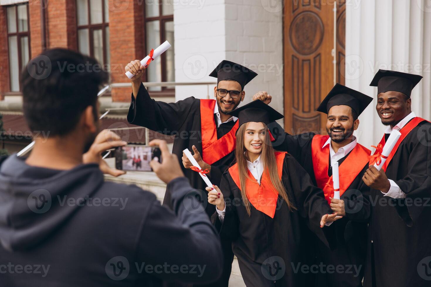 Group of Happy Graduates Celebrating Outside University with Diplomas and Taking Photos
