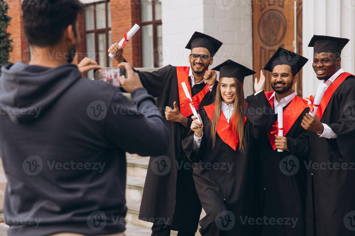 Group of Happy Graduates Celebrating Outside University with Diplomas and Taking Photos