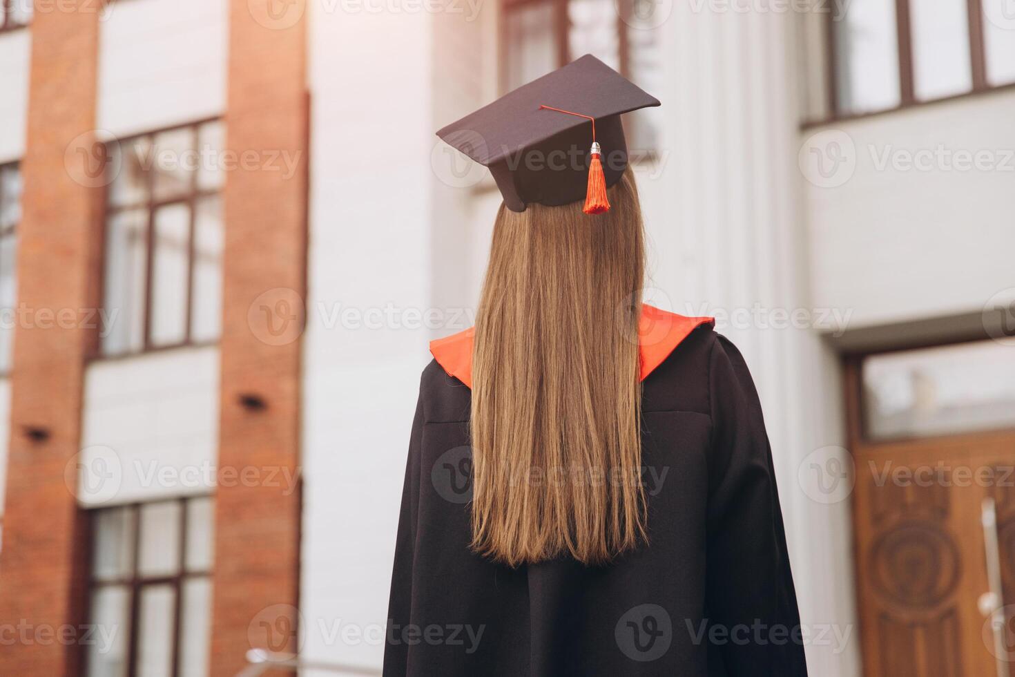 Rear View of Female Graduate in Cap and Gown Standing Outside University Building photo