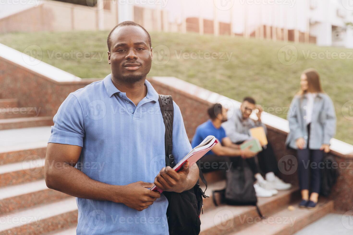 African American Confident Student Holding Books Outdoors with Friends on Campus Steps photo